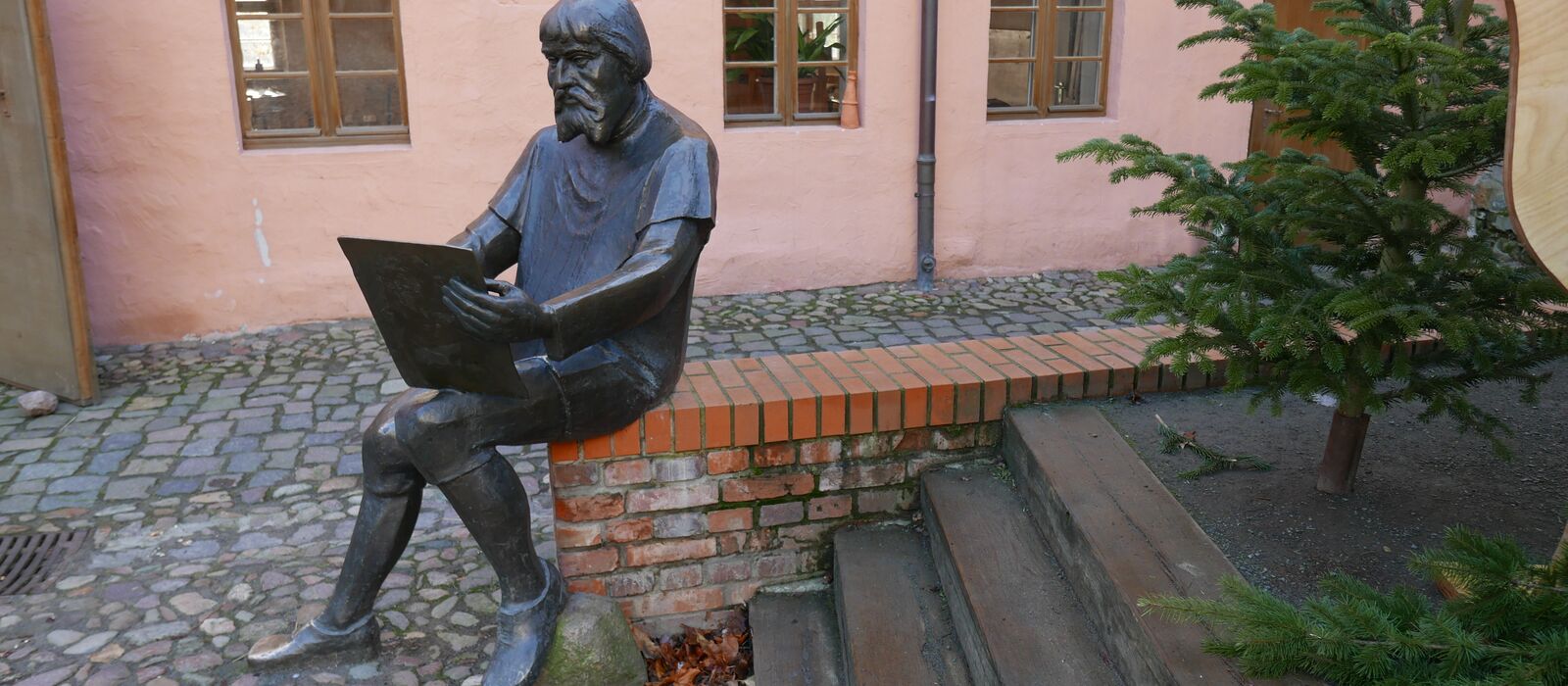Bronzeplastik eines lesenden Mannes in einem Hinterhof